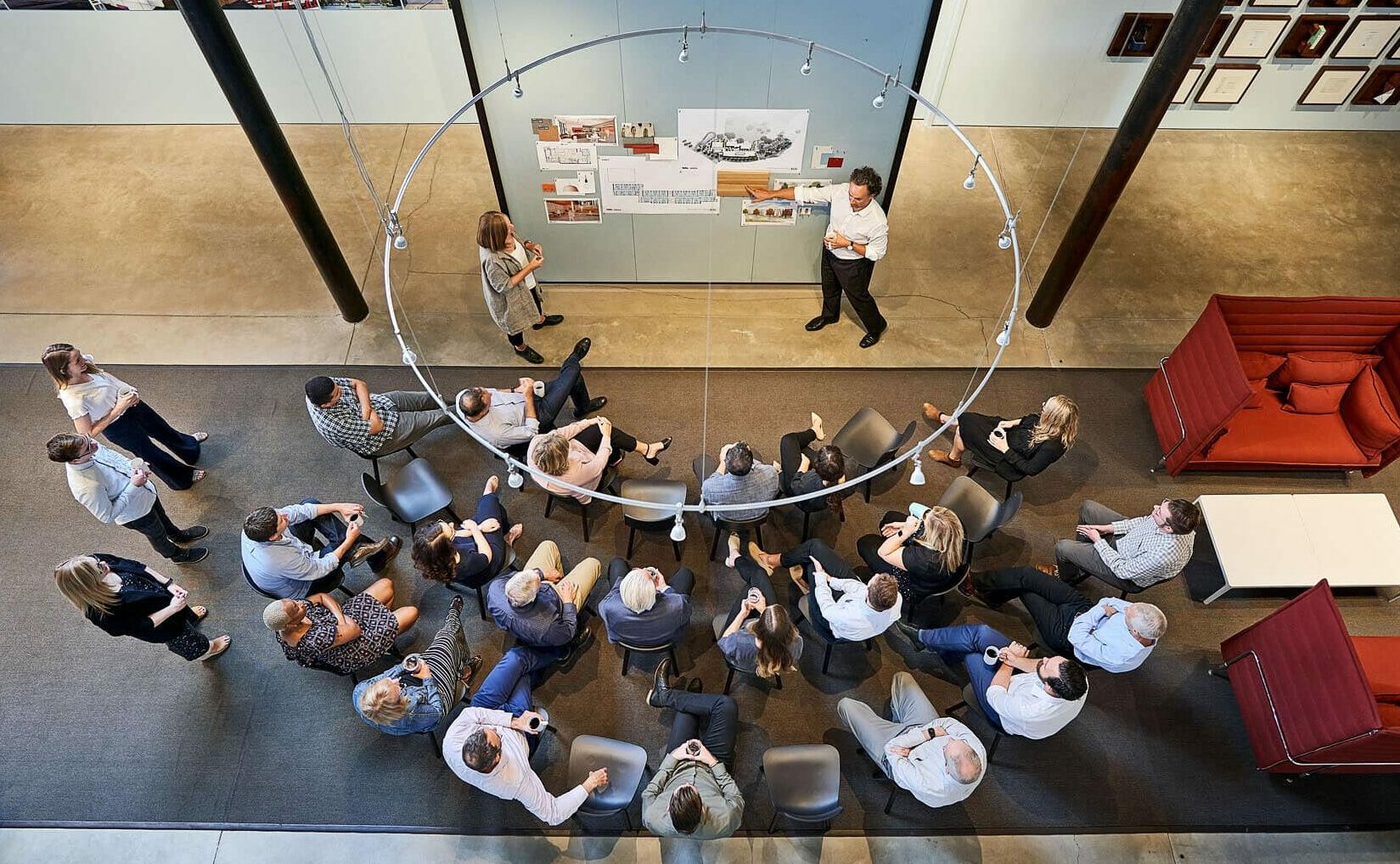 A group of employees seated around a pin-up board while others give a presentation.